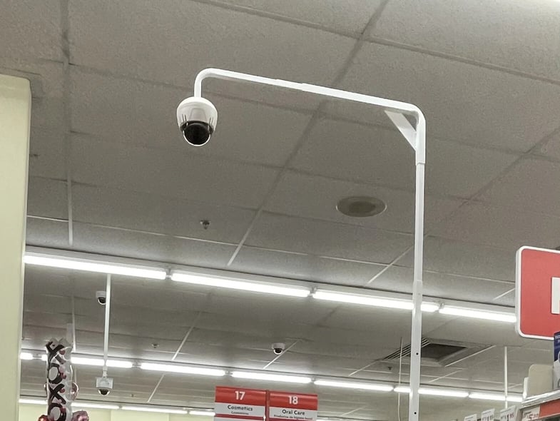 SmartDome mounted on a white pole arm in a store aisle, below the ceiling lights.